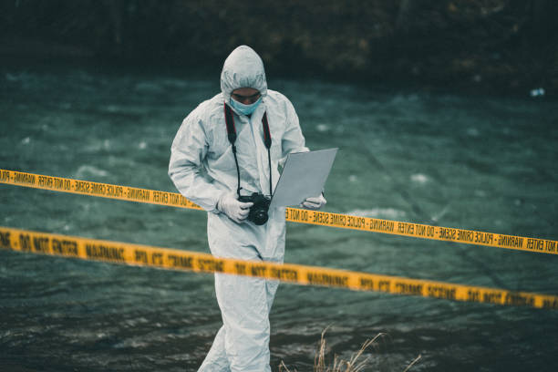 Forensic pathologist holding a ca,era looking down searching for evidence Investigator in protective suit walking through crime scene by the river fbi photos stock pictures, royalty-free photos & images