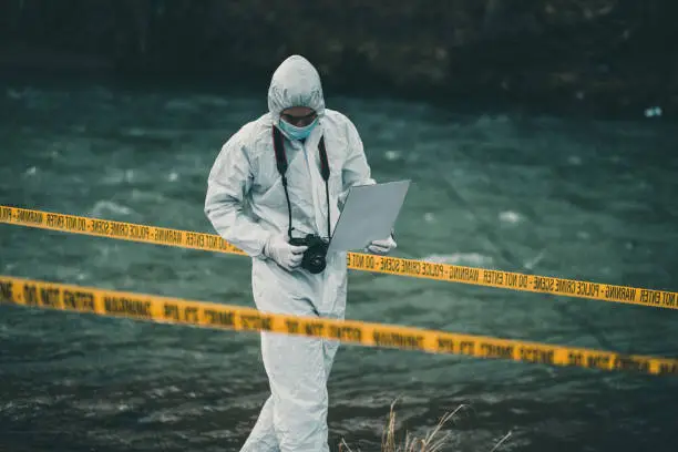 Investigator in protective suit walking through crime scene by the river