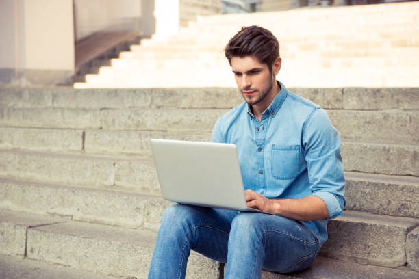 istock handsome young man sitting on the stairs and work with laptop 946043838