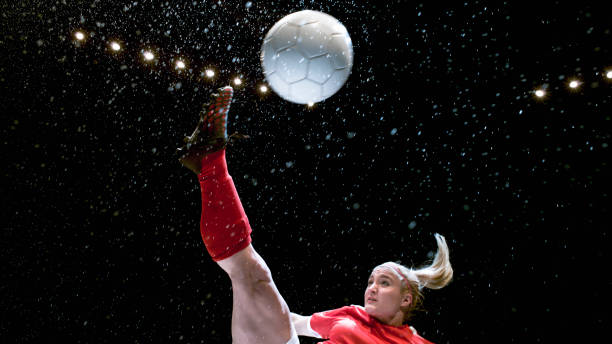 Female soccer player kicking the ball Female soccer player kicking a ball in the air against black background. football socks stock pictures, royalty-free photos & images