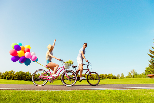 Two lovers riding bicycles with balloons on the background of sky