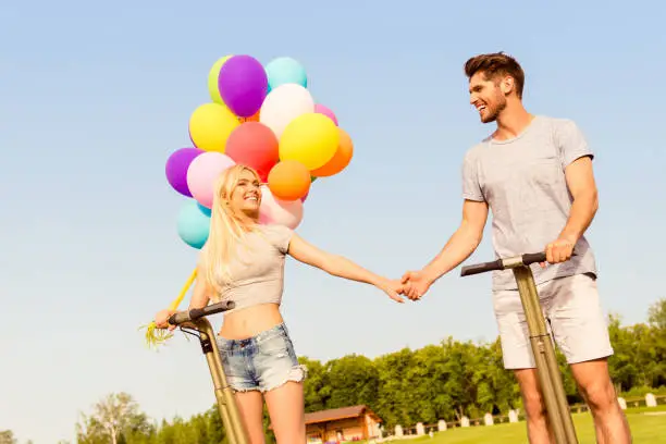 Happy lovely couple  with balloons holding hands and using segway