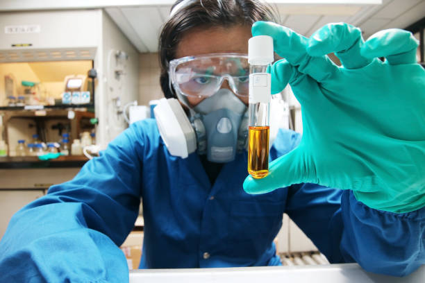 scienziato contemporaneo che analizza liquidi tossici in laboratorio. chimico sicuro che indossa tuta e respiratore che studia la provetta con liquido tossico, interno del laboratorio sullo sfondo - laboratory test tube student scientist foto e immagini stock