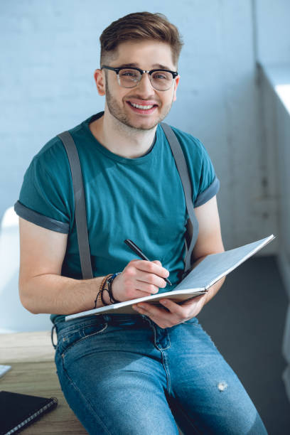 istock handsome young man in eyeglasses taking notes and smiling at camera 946118220