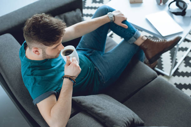 istock high angle view of young man drinking coffee while sitting on couch 946131864