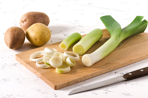 Three potatoes and leeks cut into slices on wooden plank, on white background.