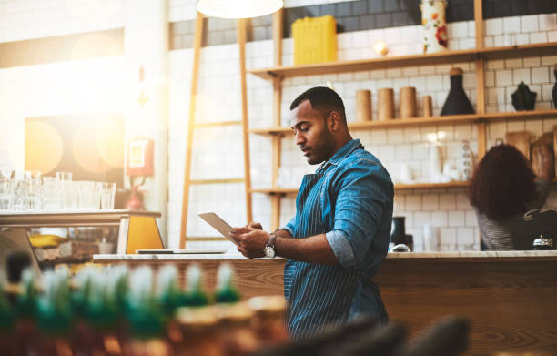 He's always making little tweaks to the business model Cropped shot of a handsome young man working on a tablet in his coffee shop cafe tablet stock pictures, royalty-free photos & images