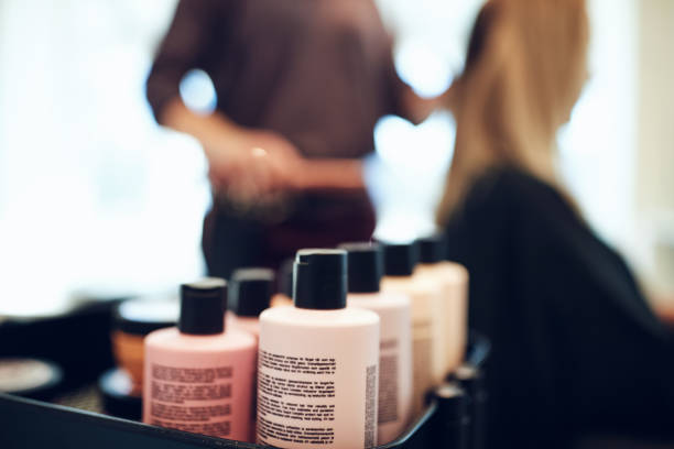 Bottles of styling products in a hair salon Closeup of shampoo and conditioner bottles on a tray in a hair salon with a hairdresser styling a client's hair in the background flaxen hair color stock pictures, royalty-free photos & images