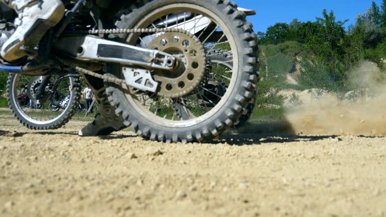 Two motorcycle starting one after another. Studded motocross wheeles starting to spin and kicking up dirt and dust. Slow motion Close up Low angle view Side view