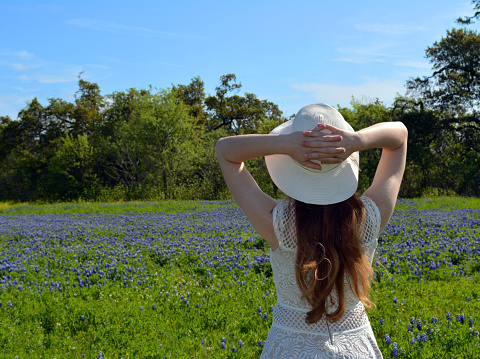 women in white hat looking away, into a field of wildflowers
