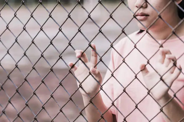 teen behind the cage or woman jailed, unhappy girl hand sad hopeless at fence prison in jail, no free and freedom struggle teen concept.