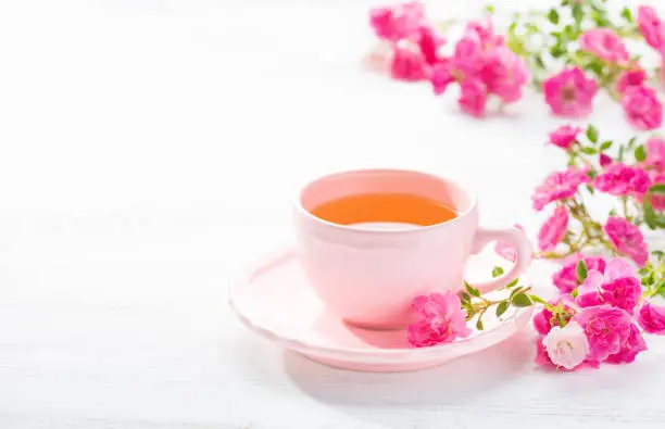 Photo of Cup of tea and branch of small pink  roses on  white rustic table.