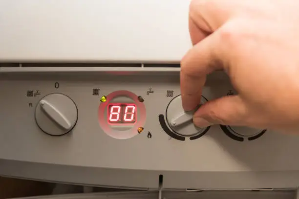 Fingers of a adult man turning on a British Combi Gas Boiler