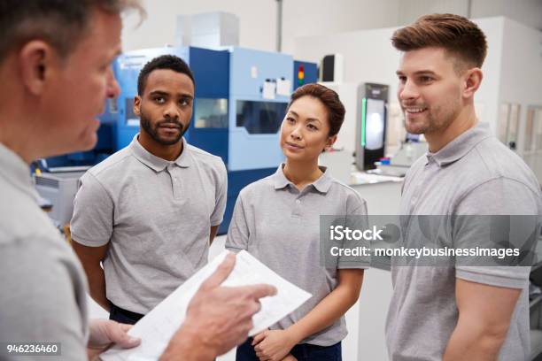 Reunión De Equipos De Ingeniería En El Piso De La Fábrica De Taller Ocupado Foto de stock y más banco de imágenes de Clase de formación