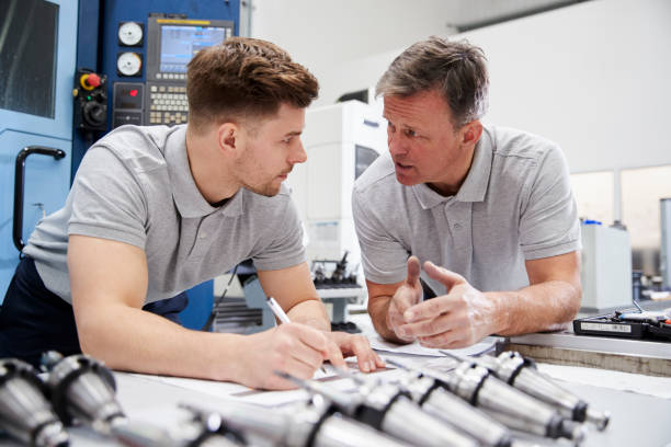 istock Engineer Showing Apprentice How To Measure CAD Drawings 946236860