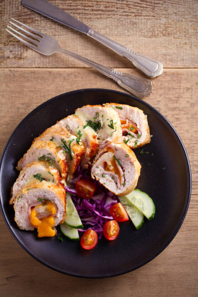 istock Chicken wrapped with ham and cheddar cheese; vegetables in black plate on wooden table 946247268