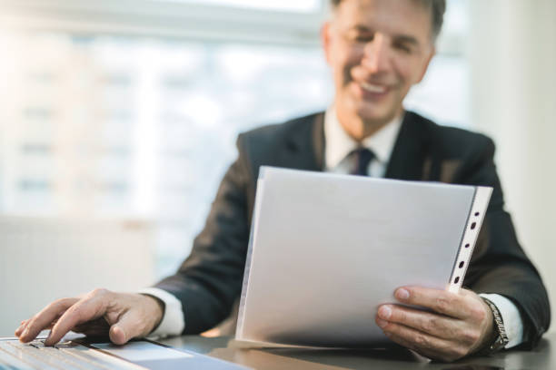 istock Cheerful mature businessman reading a document a using laptop. 946247608