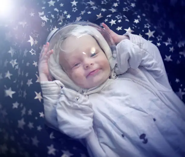 The child is in the cosmonaut's space suit. Baby lies in the stars, as if flying in space