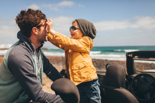 Enjoying family road trip Photo of a little boy and his father on a road trip by the seaside in their convertible car, putting sunglasses on hipster car stock pictures, royalty-free photos & images
