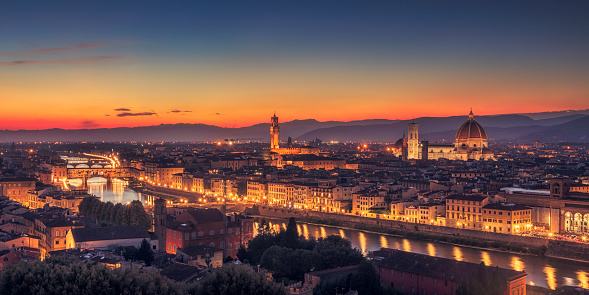 View of central Florence, Italy, in the evening. On the left is the Ponte Vecchio bridge over Arno river, center is the tower of Palazzo Vecchio (town hall), and on the right Florence Cathedral.