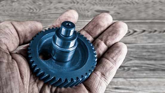Human hand holding the decorative blue gear wheel over a blurred wood background