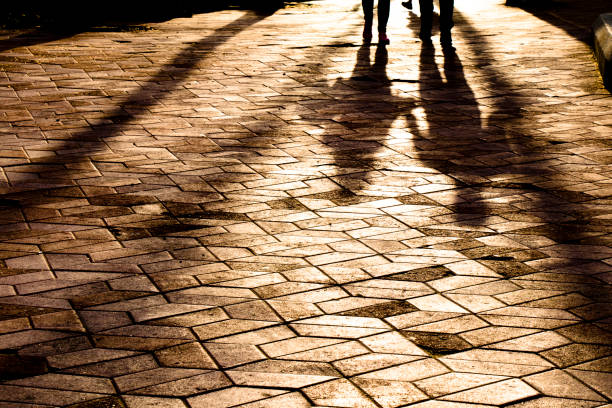 Blurry long shadows silhouettes of a couple walking on city patterned square in sunset