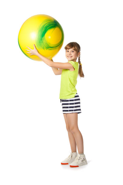 Girl with a yellow ball doing exercises on a white background. She is holding the ball in her hands