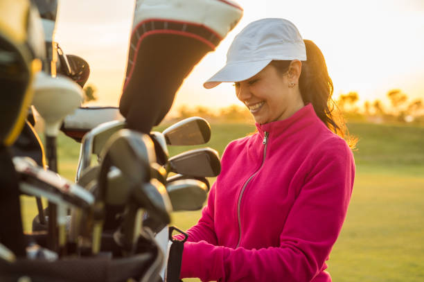 Clubes feminino golfista agarrando fora de seu saco de golfe ao pôr do sol. - foto de acervo