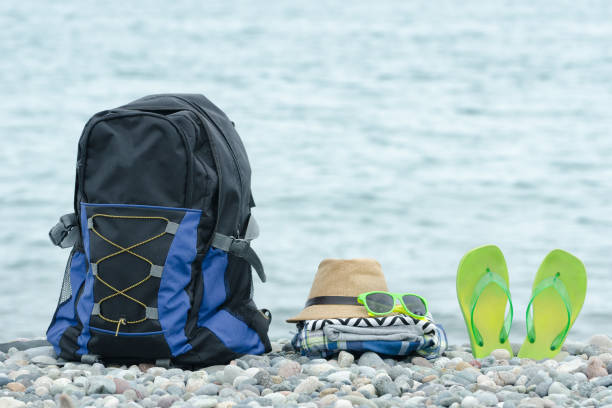 istock Backpack, hat and flip-flops on the pebble beach. Sea in the background 946365938