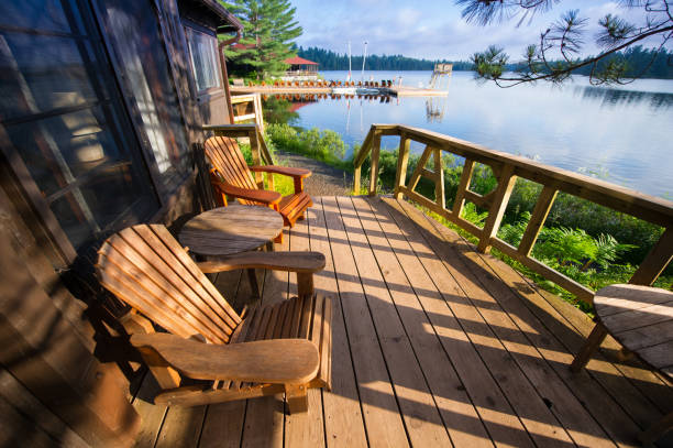 Muskoka chairs sitting on a wooden porch Muskoka chairs sitting on a wooden porch facing a calm lake. In the background there are Adirondack and Muskoka chairs on a wooden dock cottage stock pictures, royalty-free photos & images