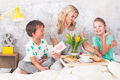 Mother´s Day - two children surprise their mother with breakfast in modern bed
