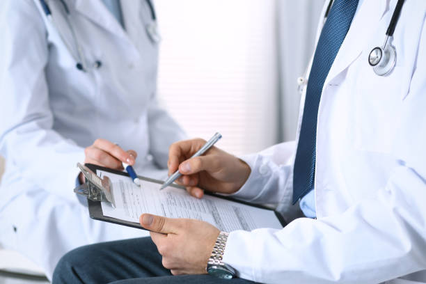 istock Two unknown doctors filling up medical form on clipboard, just hands closeup. Physicians asking question to patient or discussing medication program. Healthcare, insurance and medicine concept 946448282