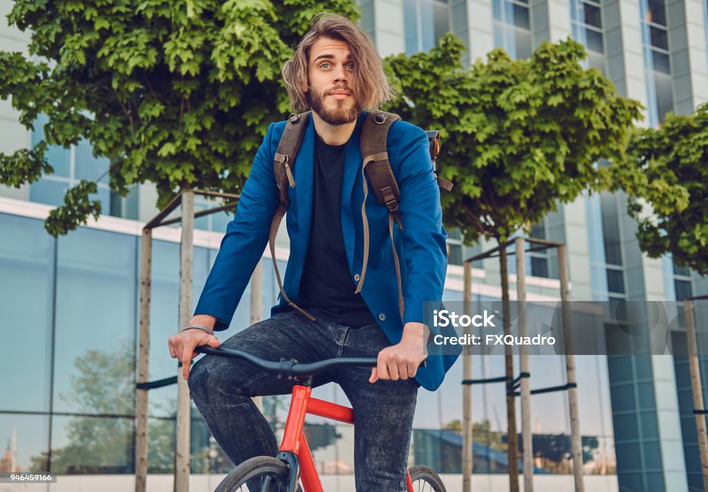 A Handsome Bearded Male With Long Hair In Stylish Clothes And A Backpack  Riding A Bicycle On The Street Outdoors Stock Photo - Download Image Now -  iStock