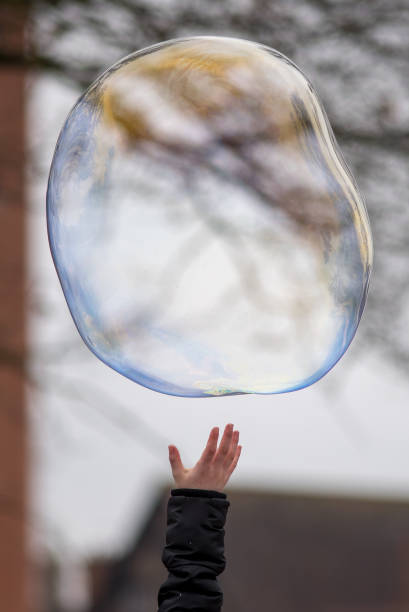 istock hand reaching up to touch bubble during the winter with tree branch in background 946465160