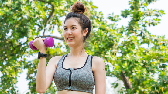 Asian cute healthy fit and firm slim girl happy to standing workout with small dumbbell in position bicep curls lifting  at outdoor garden park