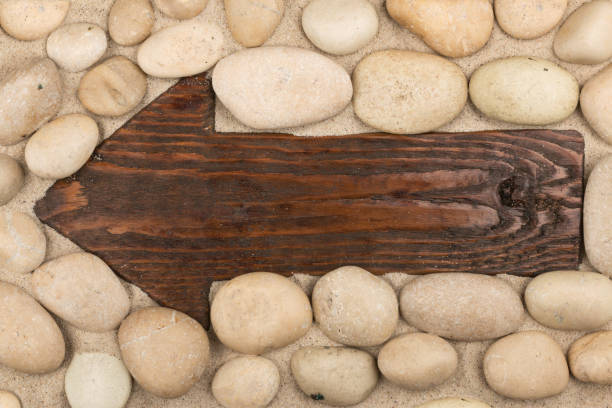 Classical wooden arrow and white stones on the sand. Space for the designer