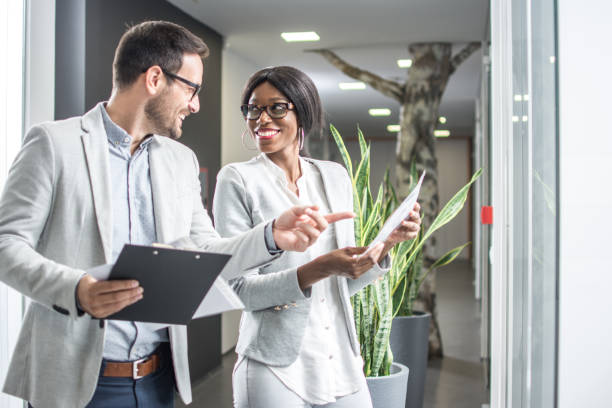 istock Two business people standing and discussing documents in office hall 946480604