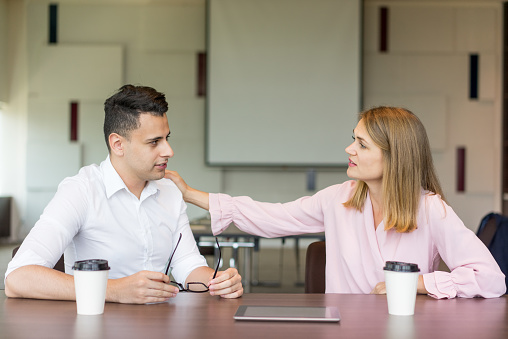 Confident businesswoman tapping male colleague on shoulder at coffee break. Young Caucasian businesswoman sitting at table with male manager, consoling or supporting him. Business relationship concept