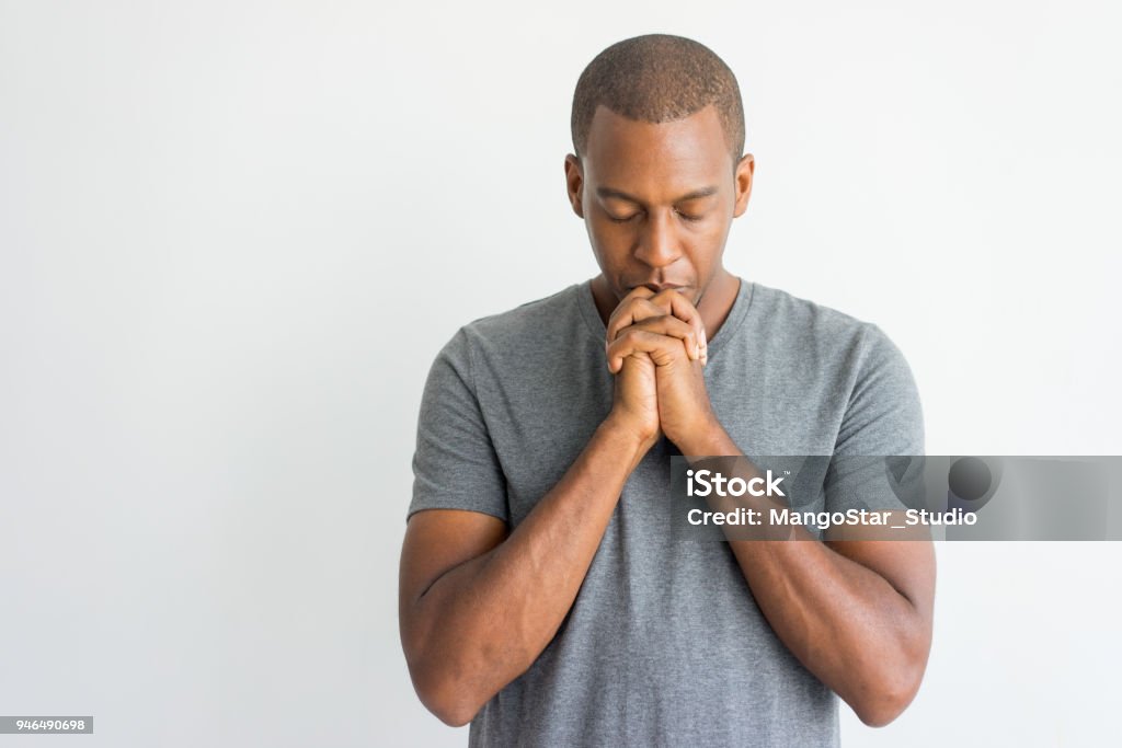 Calm spiritual handsome African guy praying with closed eyes Calm spiritual handsome African guy praying with closed eyes. Serious peaceful young man with joining hands meditating. Belief concept Praying Stock Photo