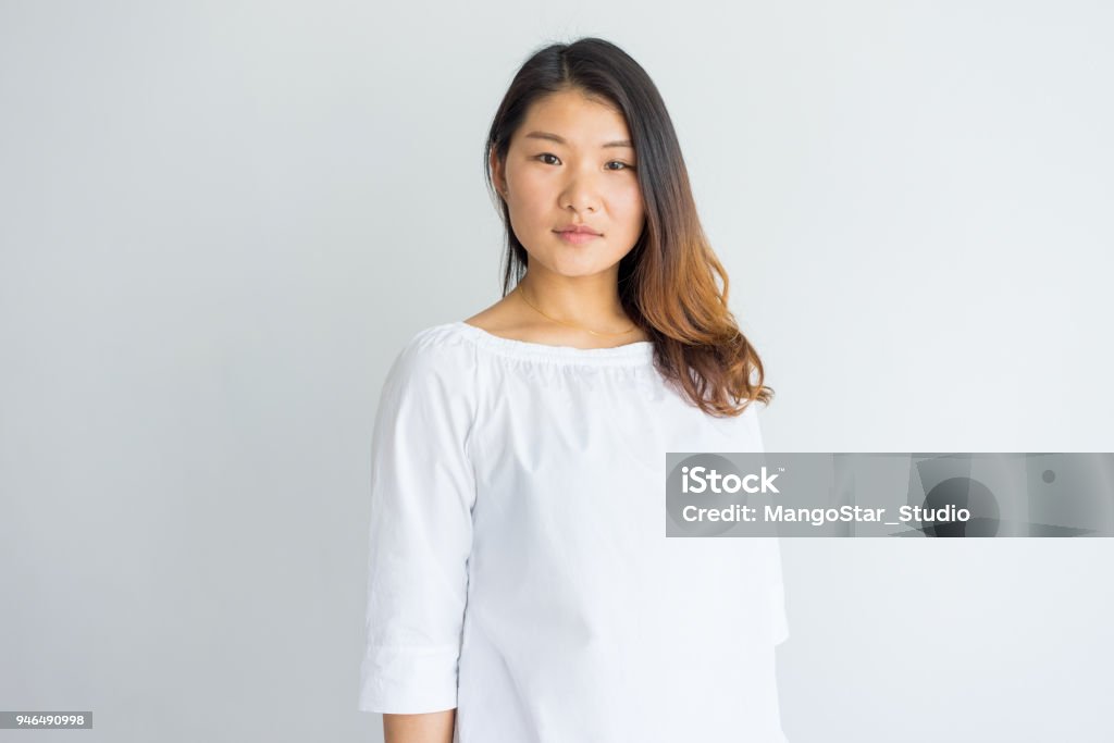 Serious beautiful young Chinese woman in white blouse Serious beautiful young Chinese woman in white blouse looking at camera. Portrait of calm confident girl with beautiful hair. Lady concept Women Stock Photo