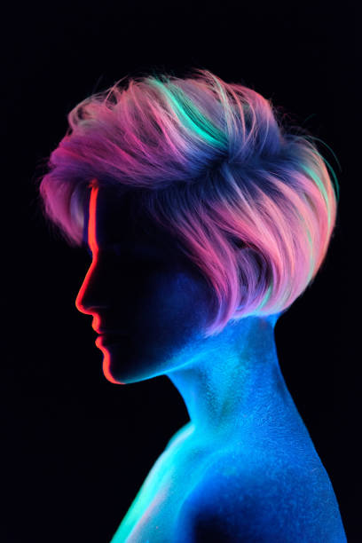 Model young beautiful girl portrait in studio with creative makeup, in neon ultraviolet lamp. Glows in the dark. Hair coloring with neon paints. Body art is blue, green, orange Young beautiful girl model with short haircut in the studio on a black background. Neon paints, makeup, body painting, colored hair coloring, creative color, poses in the light of soffits. Hands, face, blue, green, orange. fluorescent photos stock pictures, royalty-free photos & images