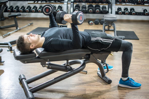 istock Handsome young man lying on exercise bench and lifting dumbbells in gym 946502276