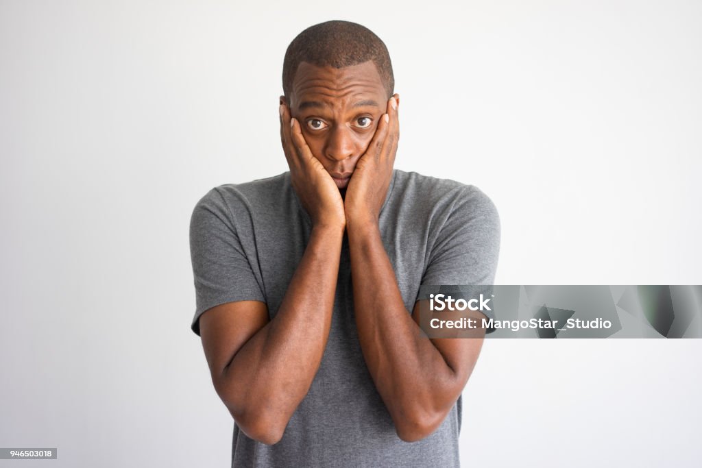 Portrait of shocked and puzzled African American Portrait of shocked and puzzled African American. Stressed black man in casual wear surprised with bad news and covering cheeks with palms. Shock and bad news concept Men Stock Photo