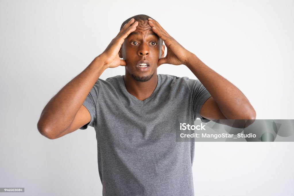 Portrait of stressed and desperate African American Portrait of stressed and desperate African American. Frightened black man in grey tshirt upset with unexpected problems and touching head. Shock and bad news concept Men Stock Photo