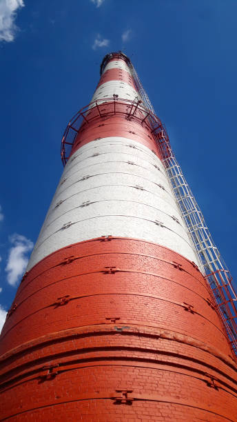 Red-white chimney of a large plant. Bottom view. On the blue sky background. Red-white chimney of a large plant. Bottom view. On the blue sky background. chicago smog stock pictures, royalty-free photos & images