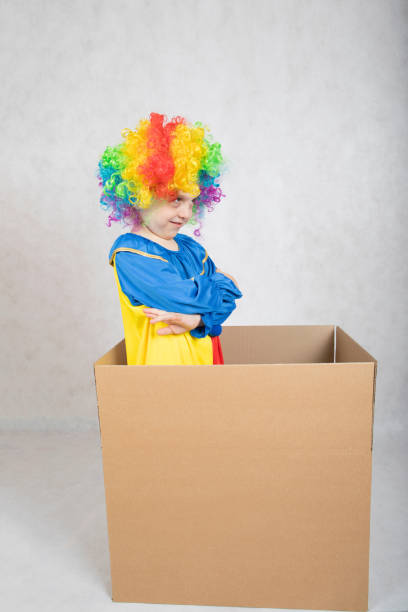 boy of five years dressed in the costume of a clown stays in a carton paper box. - clown circus telephone humor imagens e fotografias de stock