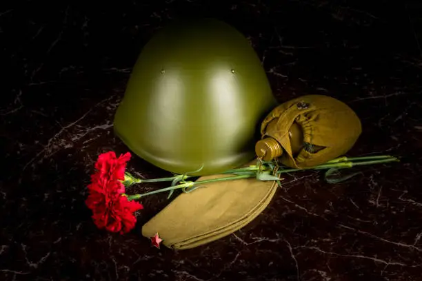 Photo of two carnations, a military helmet and a pilot's cap, a flask, against the background of the monument