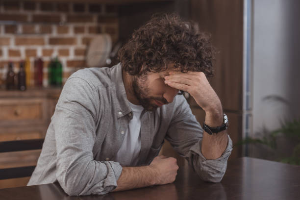 istock tired man sitting at table in kitchen and touching head 946531654