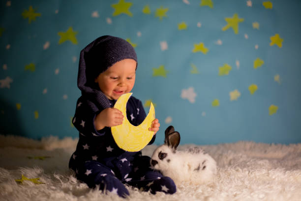 małe dziecko, chłopiec z uroczym białym króliczkiem i księżycem na niebieskim tle gwiazdy i księżyca - child bedtime imagination dark zdjęcia i obrazy z banku zdjęć