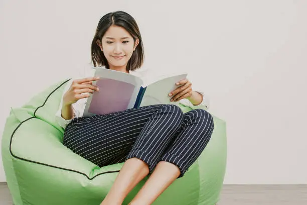 Photo of Happy Asian woman reading magazine on beanbag